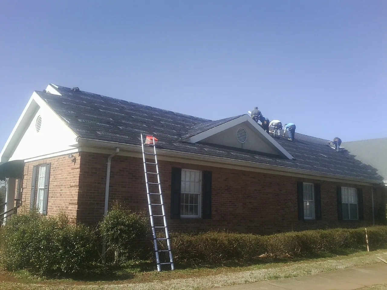 Crew tearing shingles off a brick ranch roof with a ladder set — Emergency Roof Repair work by our crew in Meriden