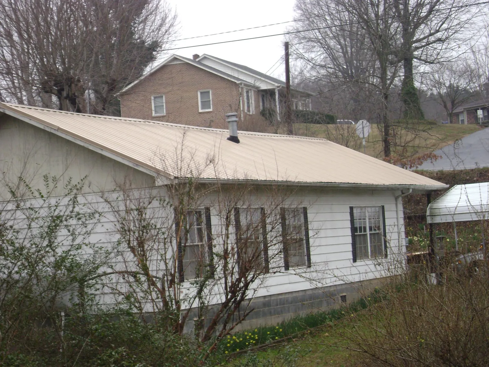Tan metal roof on a white sided house set into a hillside — Commercial Roofing by Roofing Brothers in Meriden